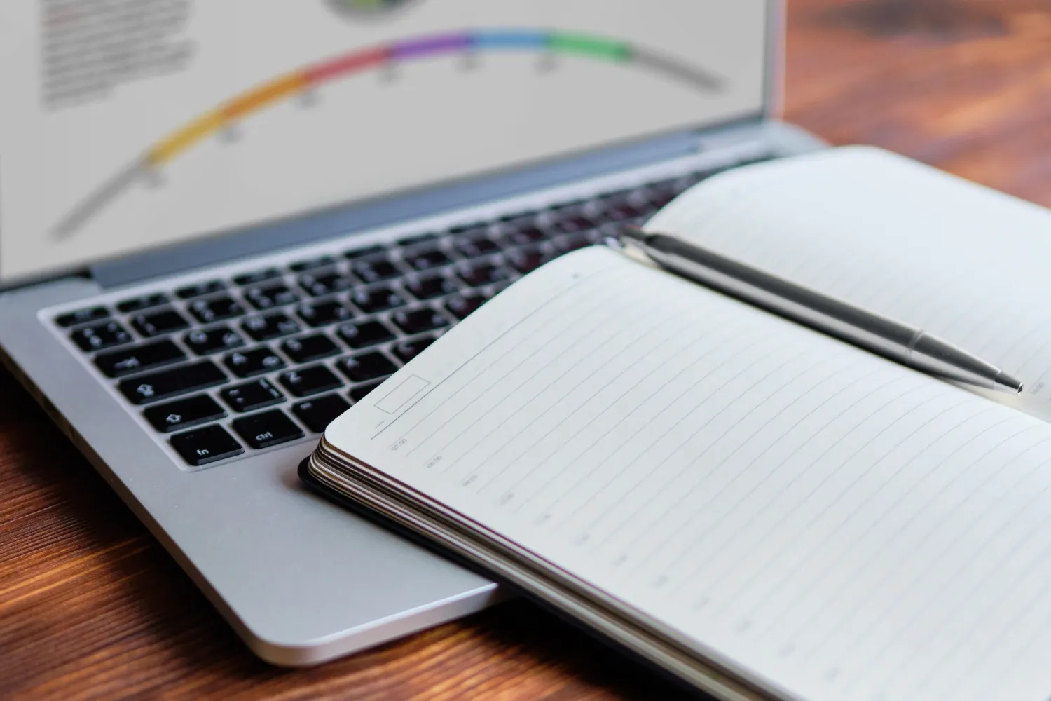 A laptop showing a profile’s scores on a coloured arc, an open notebook and a pen in front of it