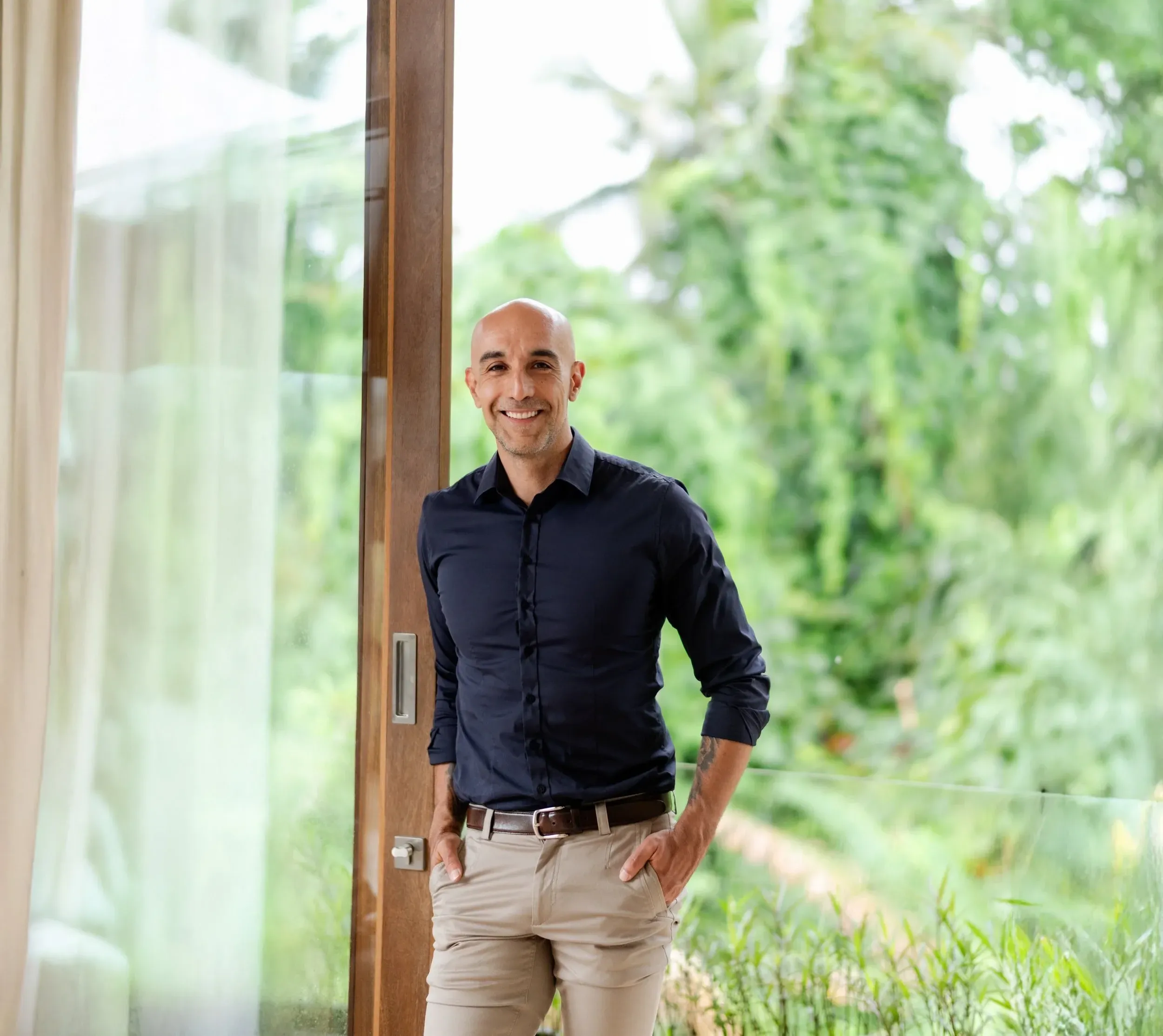Mike McGregor smiling, hands in his pockets, beside an open glass door with a garden behind him